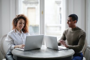 cheerful-young-couple-using-laptops-while-sitting-at-table-3967031